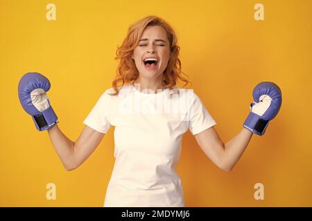 Gewinnerin Boxerin mit aufgeregt erhobenen Händen. Isoliert auf gelbem Hintergrund. Aufgeregte Frau in Boxhandschuhen. Schreiende starke junge Boxerin. Stockfoto