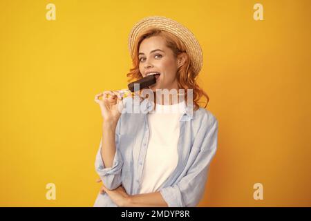 Portrait von fröhlichen lustigen Teenager-Mädchen genießt den Verzehr von kalten gefrorenen Dessert, isst köstliche Schokolade Eis, gelber Hintergrund. Stockfoto