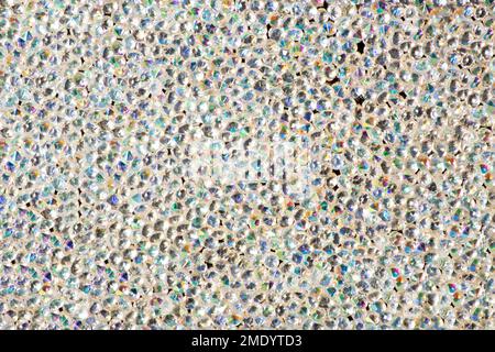 Abstrakter Strasssteinhintergrund. Textur der Strasssteine, die mit weißem Licht beleuchtet werden. Mehrfarbige glänzende Diamanten. Schließen. Leuchtfackeln auf Glas. Stockfoto