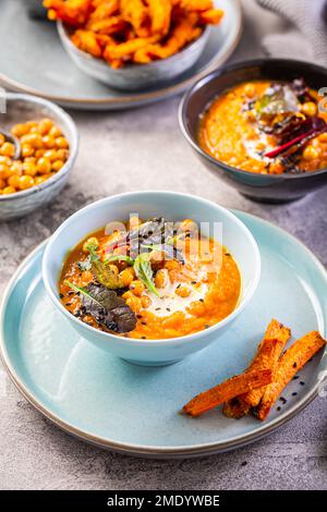 Karotten- und Süßkartoffelsuppe mit Kichererbsen und frischen Winterkräutern, Süßkartoffeln-Pommes Stockfoto