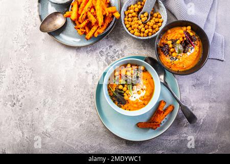 Karotten- und Süßkartoffelsuppe mit Kichererbsen und frischen Winterkräutern, Süßkartoffeln-Pommes Stockfoto