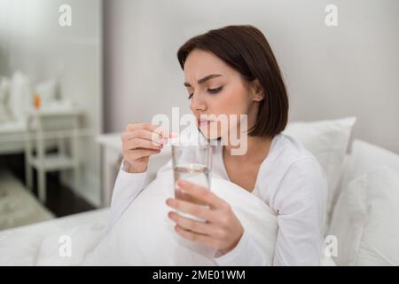 Junge Frau, die ein Glas Wasser und eine rosafarbene Kapsel in der Hand hält Stockfoto
