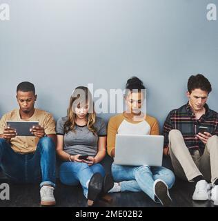Wir haben alle ein Gerät der Wahl. Studiofoto einer Gruppe junger Menschen, die drahtlose Technologie vor grauem Hintergrund verwenden. Stockfoto