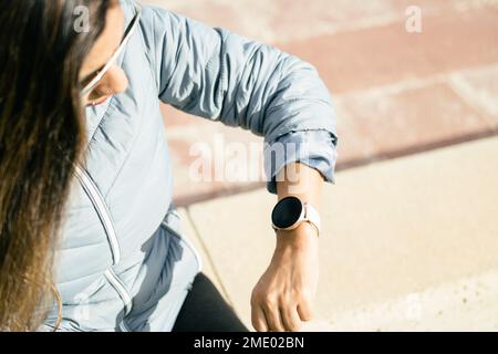 eine lateinische Frau mit langen Haaren, die auf Smartwatch schaut Stockfoto