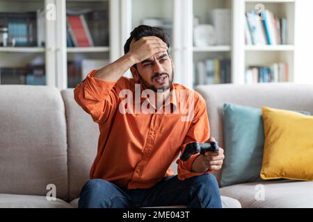 Ein trauriger araber, der zu Hause Videospiele spielt und den Joystick hält Stockfoto