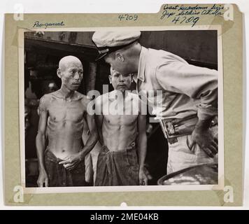 Küstenwachmänner ergreifen japanische Soldaten auf See. Dieses Bild zeigt zwei japanische Arbeiter, die in einem offenen Boot festgenommen wurden. Sie werden mit Fähnrich James R. Kennedy an Bord eines von der Küstenwache bemannten Angriffsschiffes gezeigt. Stockfoto