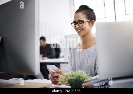 Ihre Lieblings-Business-Apps zum Laufen zu bringen. Eine junge Geschäftsfrau, die ein Mobiltelefon an ihrem Schreibtisch in einem modernen Büro benutzt. Stockfoto
