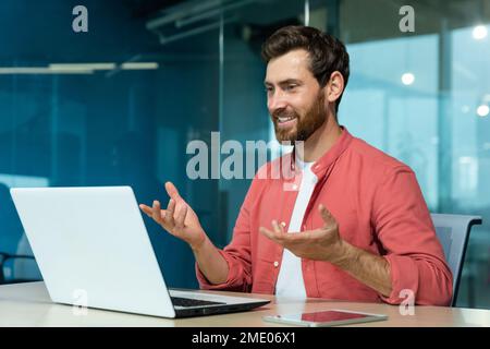 Videoanrufe von erfolgreichen und fröhlichen lächelnden Geschäftsleuten, Mann, der aus der Ferne mit einem Laptop spricht, während er im Büro sitzt, Online-Meetings mit Kollegen und Kundenbetreuung. Stockfoto