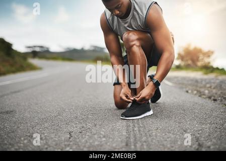 Schnürung, um in Topform zu kommen. Nahaufnahme eines sportlichen Mannes, der seine Schnürsenkel bindet, während er draußen trainiert. Stockfoto