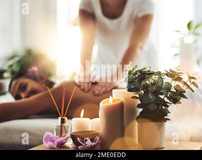 Wo sich die Welt verlangsamt. Wellness-Extras auf einem Tisch mit einer Frau, die sich im Hintergrund massieren lässt. Stockfoto