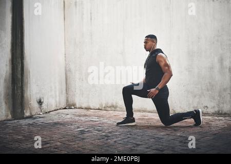 Das ist ein vollständiger Ausfallschritt. Aufnahme eines gutaussehenden jungen Mannes in voller Länge, der beim Sport im Freien Musik hört. Stockfoto