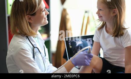 Arztin macht Ultraschall des Knies eines jungen Patienten in der Klinik. Stockfoto