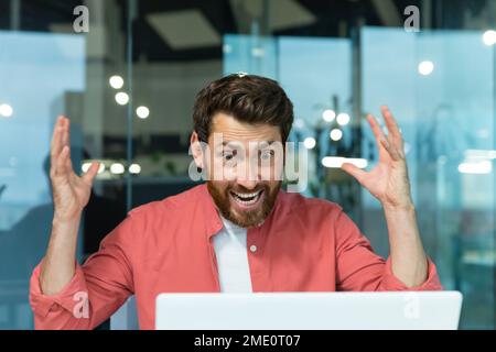 Wütender und nervöser Geschäftsmann, der per Fernzugriff per Videoanruf telefoniert, Mann, der Kollegen online anschreit, Chef im Hemd, der in einem modernen Büro mit einem Laptop arbeitet. Stockfoto