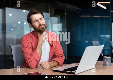Ein Mann mit Halsschmerzen arbeitet im Büro, ein Geschäftsmann bei der Arbeit hat Halsschmerzen Grippe und Erkältung, benutzt ein Notebook bei der Arbeit. Stockfoto