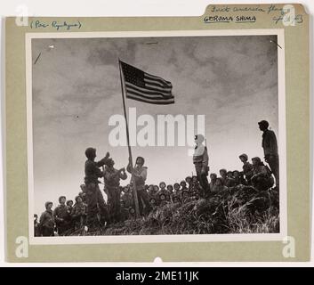 Die erste amerikanische Flagge über dem Ryukyus. Über einem Hügel auf Geruma Shima in der Keramas-Gruppe der Ryukyus heben Soldaten der 77. Division die Sterne und Streifen an – die erste amerikanische Flagge, die im japanischen Heimagium auf dem Boden gepflanzt wurde. Der Fähnrich wurde dem Kommandeur von Kompanie A, 1. Infanteriebataillon der 77. Von der Küstenwache Lieut übergeben. Richter John H., Kapitän einer von der Küstenwache bemannten LST, die Truppen in der Operation landete, einige Tage vor dem großen Angriff auf Okinawa. Das Anheben der Flagge folgte einer vergleichsweise leichten Beständigkeit gegenüber der Landung. Lieutenant Judge lebt in Belmont, Stockfoto