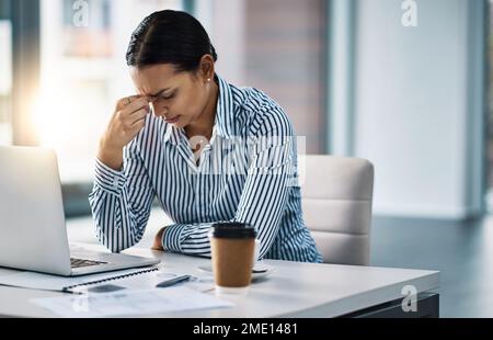 Wie kann ich mich unter all diesem Stress konzentrieren: Eine junge Geschäftsfrau, die gestresst in einem Büro arbeitet. Stockfoto