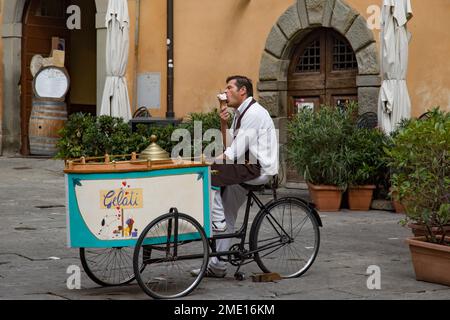 Mann sitzt auf dem Fahrrad mit mobilem Eiswagen (Snoopy Gelateria), isst Eis aus Zapfen, Cortona, Italien. Stockfoto