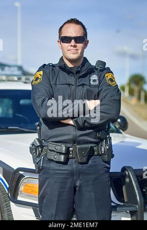 Sicherheit ist mein oberstes Anliegen. Das ganze Porträt eines gutaussehenden jungen Polizisten, der auf Patrouille mit gekreuzten Armen stand. Stockfoto