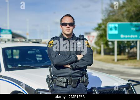 Vertrau mir, diese Stadt zu beschützen. Verkürztes Porträt eines gutaussehenden jungen Polizisten, der auf Patrouille mit gekreuzten Armen stand. Stockfoto