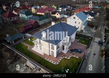 Draufsicht auf ein Wohnhaus mit Photovoltaik-Solarpaneelen, umgeben von Hof, Straße und Familienwohnungen. Häuser, Häuser, Straßen und Gebäude in einem neuen Bezirk oder einer Vorstadt. Stockfoto