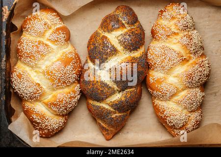 Hausgemachtes traditionelles Challah-Brot auf Backpapier, dekoriert mit Sesam- und Mohnsamen. Jüdische Küche. Challah für Sabbat Stockfoto