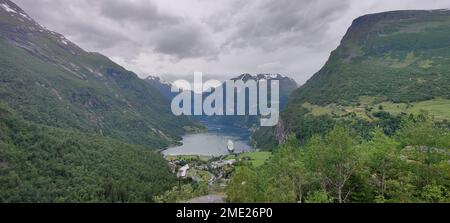 Ein großes Schiff im Wasser des Fjords, umgeben von den großen Bergen mit verschneiten Gipfeln an einem düsteren Tag Stockfoto