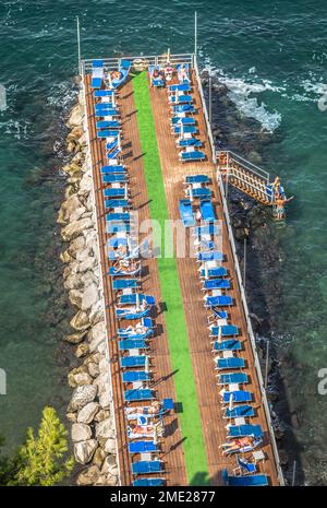 Sonnenanbeter und Liegestühle standen auf einem Pier in Sorrent, Kampanien, Italien. Stockfoto