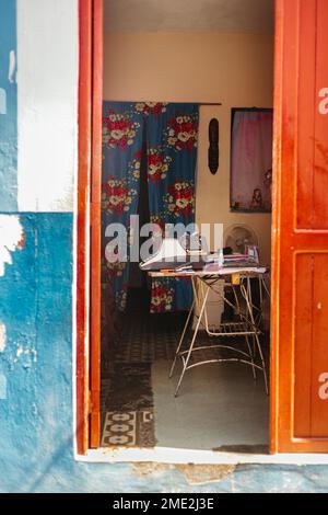 Innendesign des alten Hauses mit Zimmertür und Tisch aus Holz mit Dingen und Instrumenten in der Nähe von altmodischen Vorhängen mit Blumenmuster Stockfoto