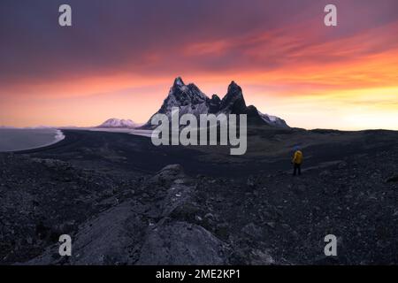 Unbekannter Tourist, der an einem stürmischen Tag in Eystrahorn, Krossanesfjall, Island, in der Nähe der Küste vor dem Sonnenuntergang stand Stockfoto