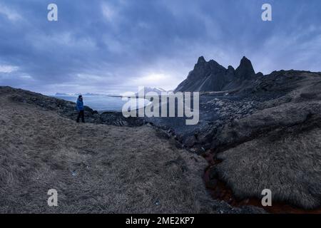 Unbekannter Tourist, der an einem stürmischen Tag in Eystrahorn, Krossanesfjall, Island, in der Nähe der Küste vor grauem Himmel stand Stockfoto