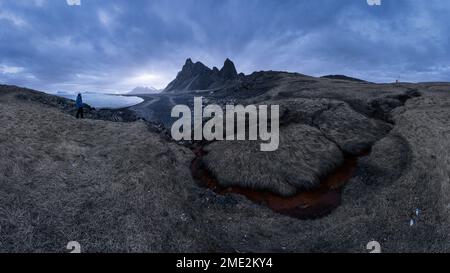 Unbekannter Tourist, der an einem stürmischen Tag in Eystrahorn, Krossanesfjall, Island, in der Nähe der Küste vor grauem Himmel stand Stockfoto