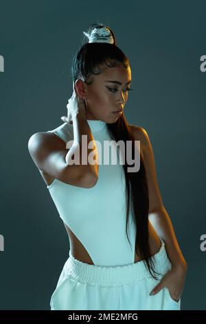 Junge Frau in weißem Body und Hose, die im Studio vor grünem Hintergrund steht Stockfoto
