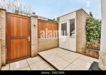 Moderne Holztür eines Wohnhauses auf dem Land mit Ziegelzaun und kleinem Lagerraum im Freien mit Bodenfliesen Stockfoto