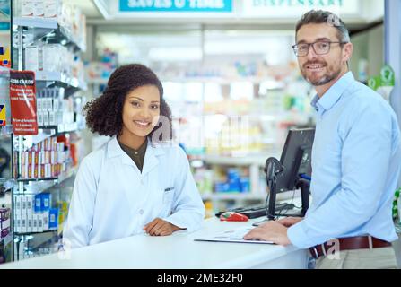 Meine Kunden gehen immer mit einem Lächeln. Gekürztes Porträt einer attraktiven jungen Apothekerin, die einem männlichen Kunden in der Apotheke hilft. Stockfoto