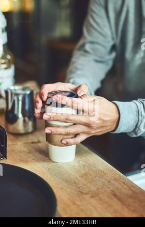 Frisch und schnell serviert. Nahaufnahme eines unbekannten Baristas, der eine Tasse frisch gebrühten Kaffees in einem Café schließt. Stockfoto