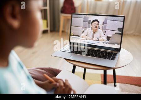 Nahaufnahme eines asiatischen Lehrers, der auf einem Laptop-Bildschirm in einer Online-Lektion spricht, während ein Kind von zu Hause aus lernt Stockfoto