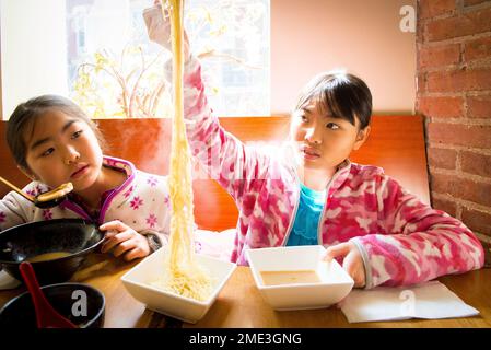 Asiatisches Mädchen isst Ramen in einem Restaurant vor Ort - streckt lange Nudeln in der Luft Stockfoto