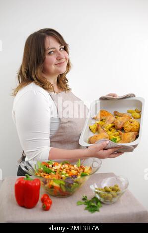 Lächelnde junge Frau, die frischen Salat auf dem Teller serviert. Fröhlich lächelnde süße Frau kocht frischen, gesunden veganen Salat zu Hause mit viel Gemüse in der Küche und probiert neues Rezept High Quality Foto Stockfoto