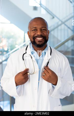Vertikales Porträt eines lächelnden afroamerikanischen Arztes im Krankenhauskorridor Stockfoto