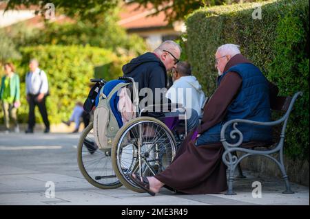 Katholisches Geständnis – ein Mann im Rollstuhl gesteht einem katholischen Priester, einem Franziskaner, in Medjugorje. Stockfoto