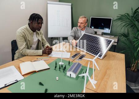 Geschäftsleute diskutieren über Solarpaneele am Tisch im Büro Stockfoto