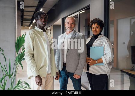 Selbstbewusster, reifer Geschäftsmann, der mit jungen Kollegen im Amt steht Stockfoto