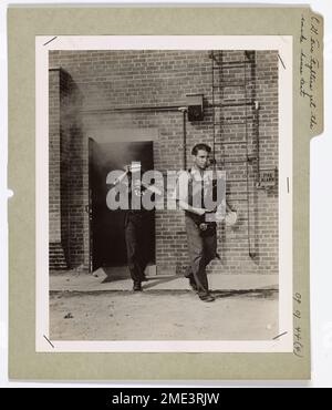 Dieses Bild zeigt zwei Küstenwächter, die aus dem Smoke House der Fire Fighting School in Fort McHenry, Baltimore, Maryland auftauchen. Sie absolvieren Schulungen, um auf Brandfälle auf Schiffen und in maritimen Umgebungen zu reagieren. Stockfoto