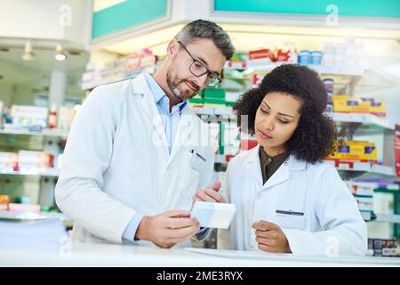 Seine pharmazeutische Expertise weiterzugeben. Ein reifer Mann und eine junge Frau diskutieren Medikamente während der Arbeit in einer Apotheke. Stockfoto