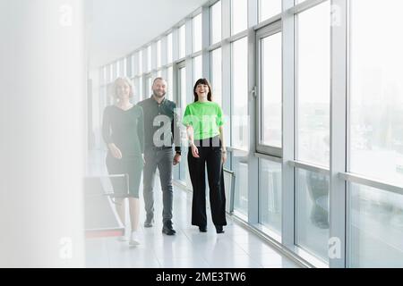 Drei glückliche Geschäftsleute in grüner Kleidung, die auf dem Büroboden herumlaufen Stockfoto