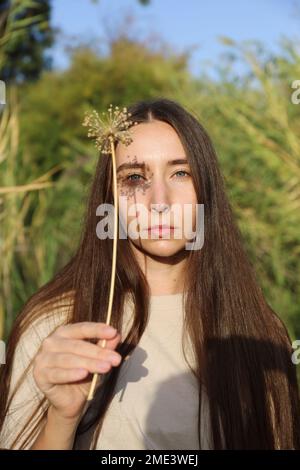Junge Frau, die an sonnigen Tagen getrocknete Blumen in der Hand hält Stockfoto