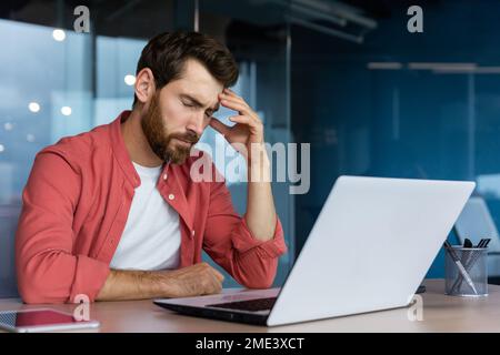 Frustrierter Geschäftsmann deprimiert am Arbeitsplatz, der an einem Laptop arbeitet, Mann im Hemd verärgert und traurig verärgert über schlechte Arbeitsergebnisse und Leistungen im Büro. Stockfoto