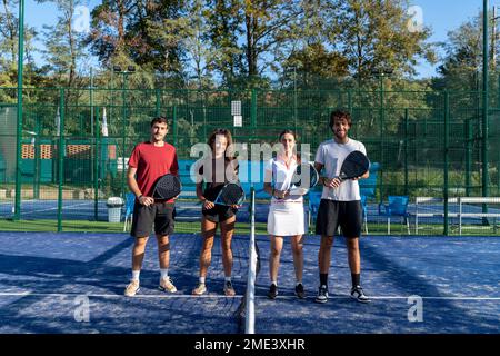 Glückliche Männer und Frauen mit Tennisschlägern auf dem Sportplatz Stockfoto