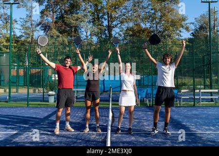 Glückliche Männer und Frauen mit erhobenen Armen auf dem Sportplatz Stockfoto