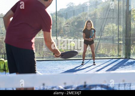 Ein junger Mann, der mit einer Frau am sonnigen Tag Paddeltennis spielt Stockfoto